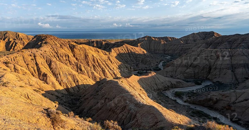 Canyon runs through a landscape of eroded hills at sunrise, Badlands, Issyk Kul Lake in the background, Canyon of the Forgotten Rivers, Issyk Kul, Kyrgyzstan, Asia