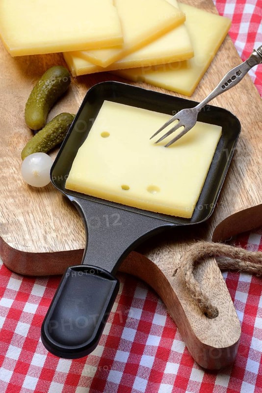 Raclette, cheese slices on wooden board and in raclette pans, Switzerland, Europe
