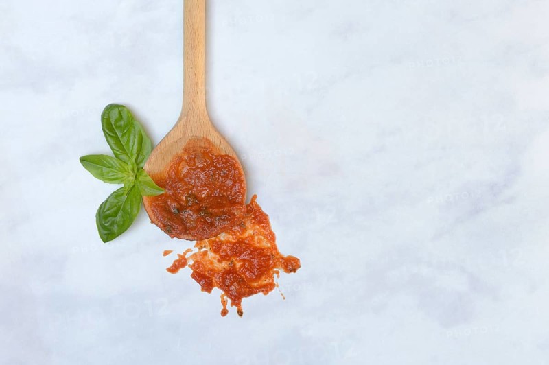 Cooking spoon with tomato sauce and basil leaf