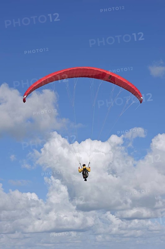 Paraglider in flight with red wing, canopy against blue cloudy sky, Brittany, France, Europe