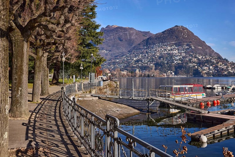 Lakeside promenade, railing with shade, trees, lake, mountain, mist, blue sky, Lake Lugano, Lugano, district Lugano, canton Ticino, Switzerland, Europe