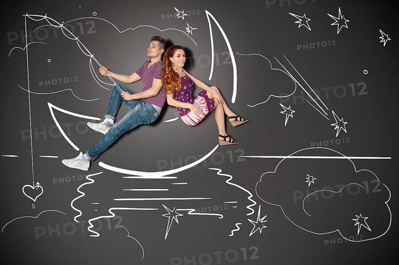 Happy valentines love story concept of a romantic couple fishing on a moon with a heart on a hook against chalk drawings background