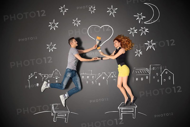 Happy valentines love story concept of a romantic couple standing on a stool and painting a heart in the night sky against chalk drawings background