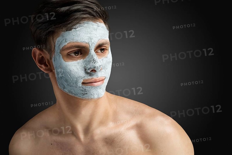 Portrait of a beautiful, relaxed young man with a face mask made of clay, skin care for face and body