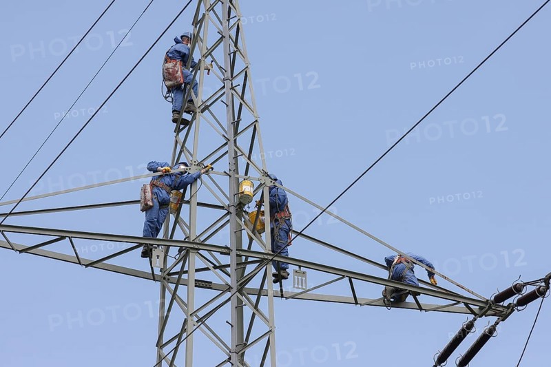 Industrial climber high up on an electricity pylon, workers wearing protective clothing, blue sky, Germany, Europe
