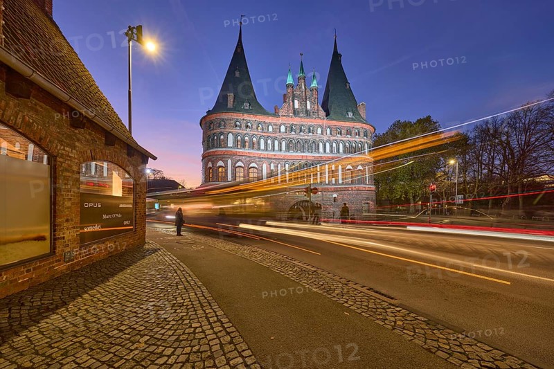 City gate Lübeck Holstentor, historic brick building, footpath and cycle path, light traces of a public bus, motion blur, evening blue hour, street Holstentorplatz, Hanseatic city of Lübeck, independent city, Schleswig-Holstein, Germany, Europe