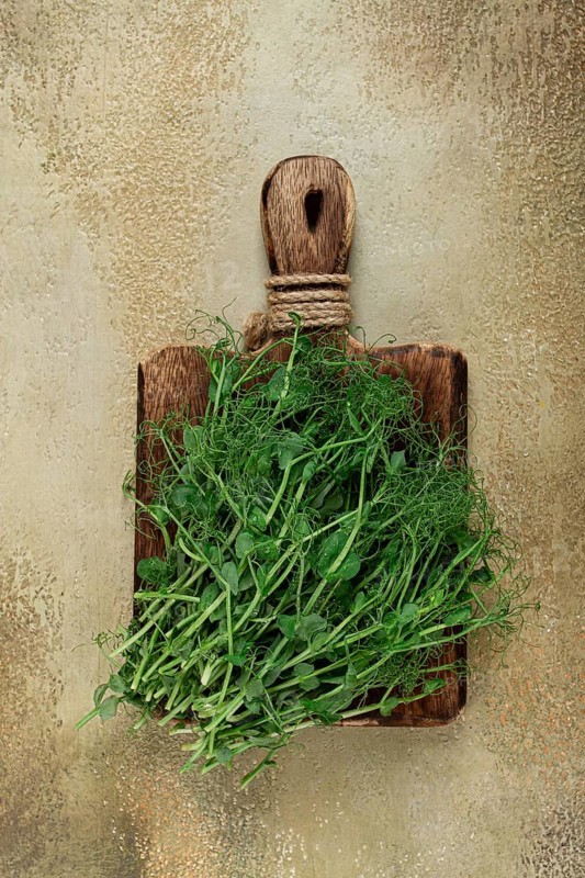 Lush green herbs are arranged on a wooden cutting board, showcasing their vibrant color and fresh appearance against a textured background, ideal for culinary use.