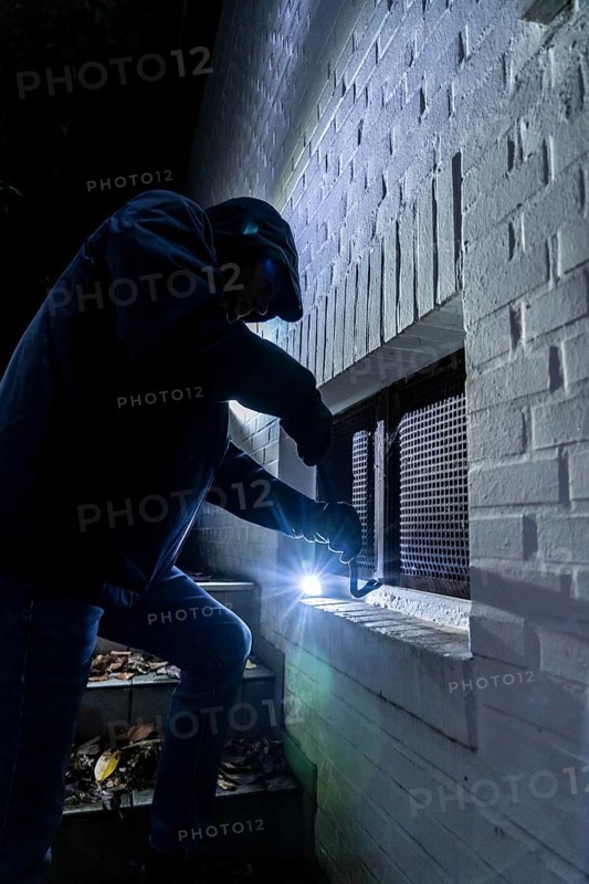 Symbolic image of a house burglary, perpetrator has approached a house from the garden side and tried to break open a cellar window to get into the flat
