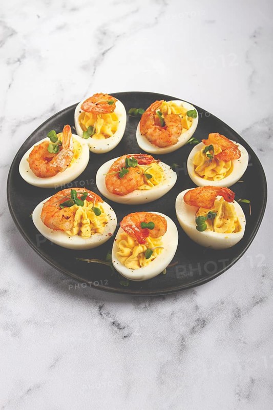 Boiled eggs stuffed with yolk and seasoned with mayonnaise, stuffed eggs with shrimp, on a black plate, selective focus, close-up, no people