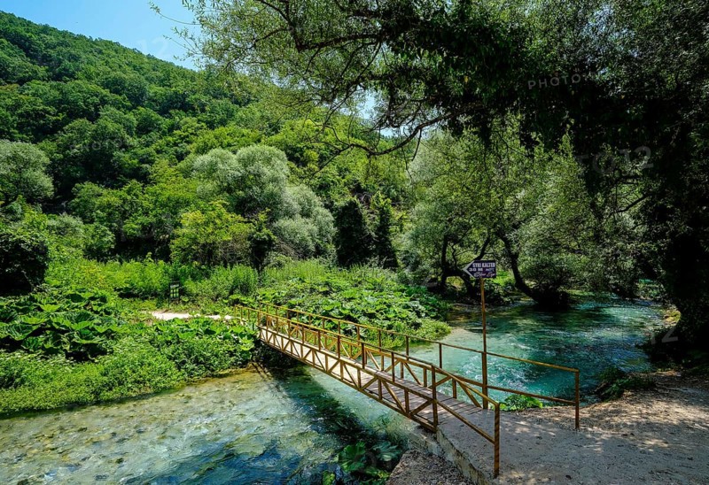 Muzina, Albania, Syri i Kaltër, BLUE EYE, is the country's most water-rich spring at 6 metres per second. The water emerges from a spring pot at a depth of more than 50 metres under high pressure. The water temperature is a fairly constant 12.75°C. The Blue Eye is located midway between the larger towns of Saranda on the coast and Gjirokastra inland. Sign over a bridge to the spring pot 30 metres away, Europe