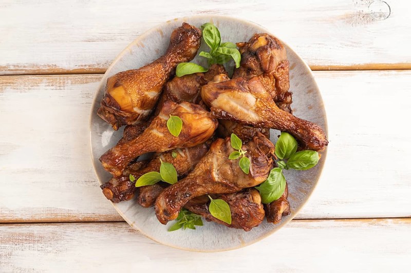 Smoked chicken legs with herbs and spices on a ceramic plate on a white wooden background. Top view, flat lay, close up