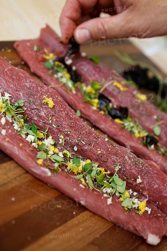 Swabian cuisine, preparation of lamb with prunes, raw lamb stuffed with herbs, rosemary, sliced garlic, lemon zest, fillets on wooden board, grandmother's cooking, regional, home cooking, typical Swabian, traditional cuisine reinterpreted, food photography, men's hands, studio, Germany, Europe