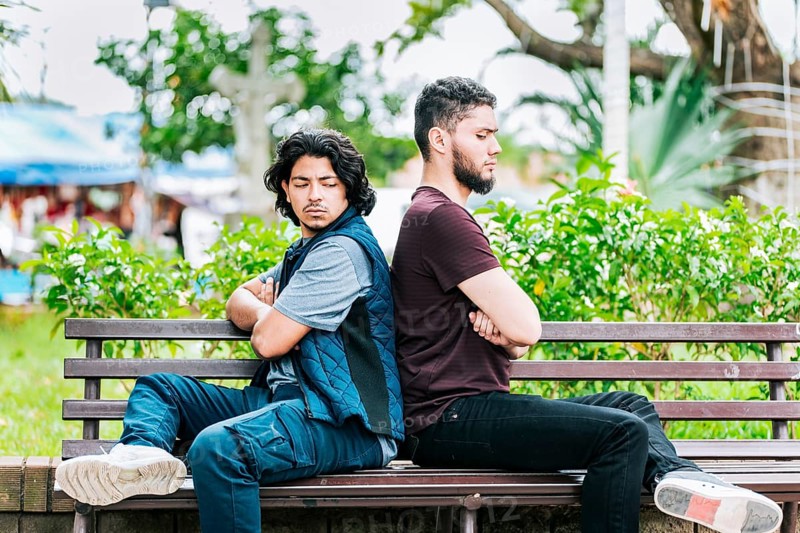Two angry friends sitting on a park bench. Two friends arguing on a park bench