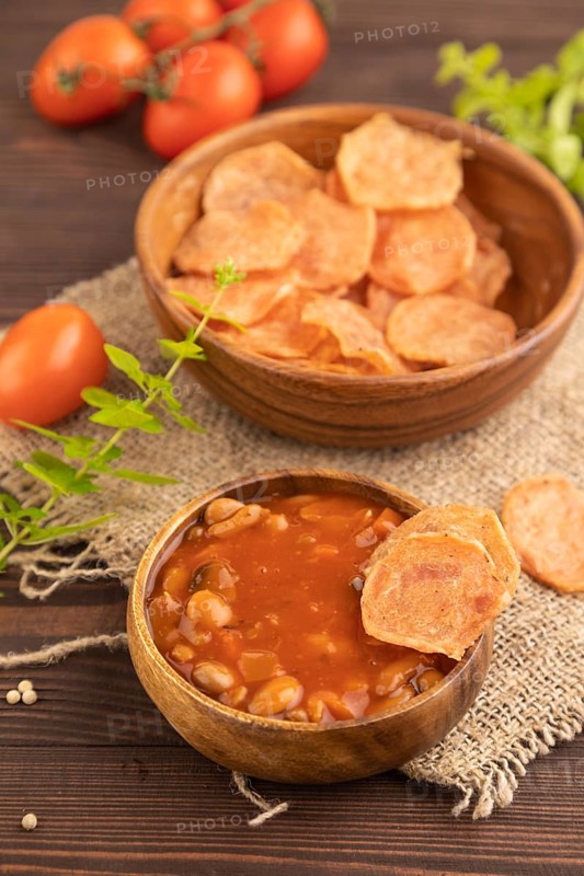 Slices of dehydrated salted meat chips with herbs and spices on brown wooden background and linen textile. Side view, close up, selective focus
