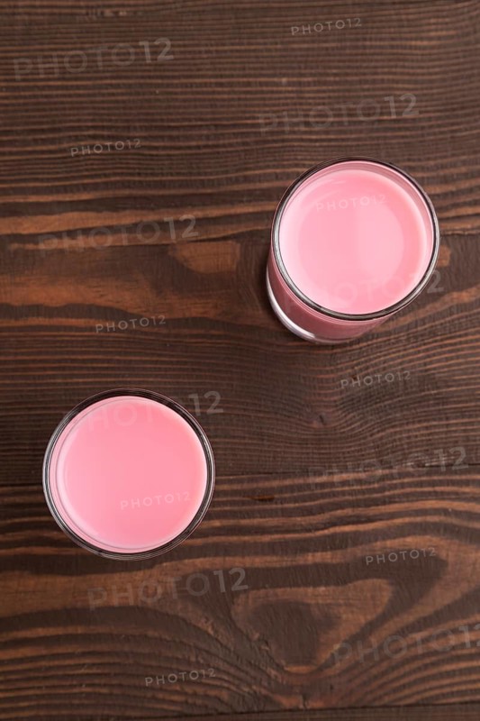 Sweet strawberry liqueur in glass on a brown wooden background. top view, close up, flat lay