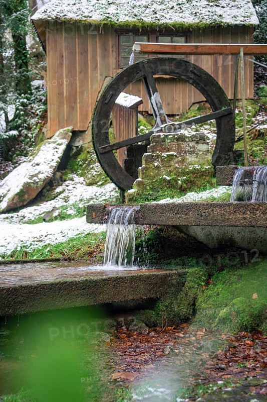 An old water wheel turns next to a hut with snow and running water, spa garden, Bad Wildbad, Black Forest, Germany, Europe