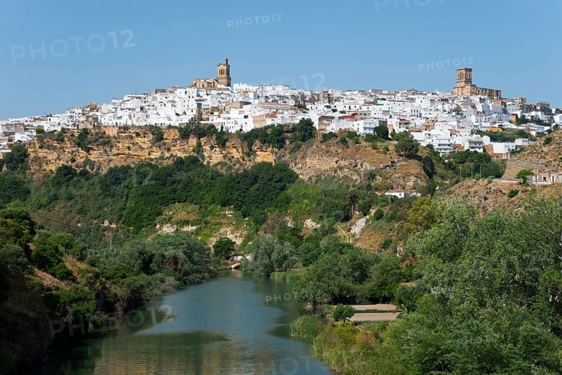 Whitewashed houses on a green hill along a river under a clear sky, Arcos de la Frontera, Guadalete river, Cadiz province, Cadiz, Andalusia, Spain, Europe