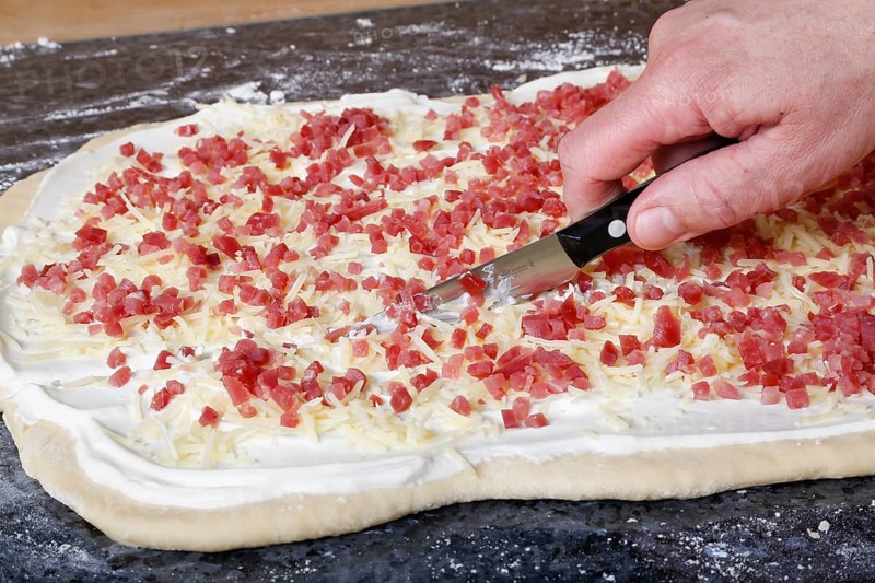 Swabian cuisine, preparation of savoury yeast plait with smoked meat, salty wreath bread, yeast yeast dough pastries, cutting raw yeast dough with bacon cubes, grated cheese, sour cream, grandmother's kitchen, regional, home cooking, typical Swabian cuisine reinterpreted, traditional cuisine reinterpreted, men's hands, food photography, studio, Germany, Europe