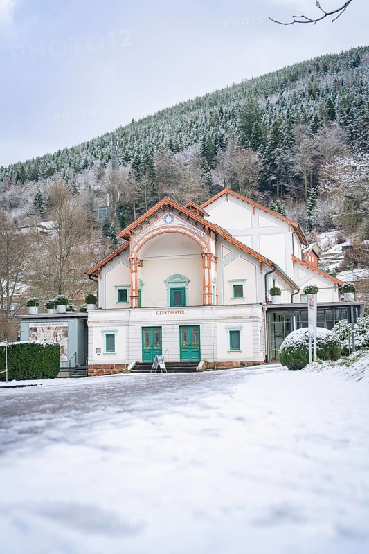 A snow-covered theatre building against a wooded mountain backdrop in winter, Königliches Kurtheater, Bad Wildbad, Black Forest, Germany, Europe