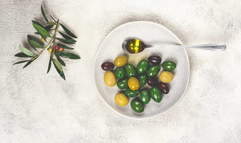 A mix of olives, a variety of Chalkidiki, verdi giganti and Kalamata, on a plate with a spoonful of olive oil, top view, no people