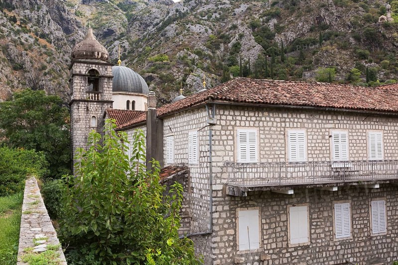 Old two storey stone building with white storm shutters on windows and covered with traditional terracotta clay roof tiles plus domes of Orthodox Churches, Old Town of Kotor, Montenegro, Europe