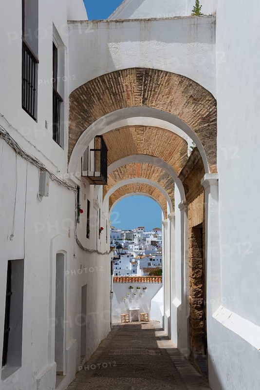 Narrow passageway with arches and white facades in a Mediterranean town in the sunshine, view through the arches of the Iglesia del Convento de la Conceptión, Museo Convento to the new town, Vejer de la Frontera, Province of Cadiz, Cadiz, Andalusia, Spain, Europe