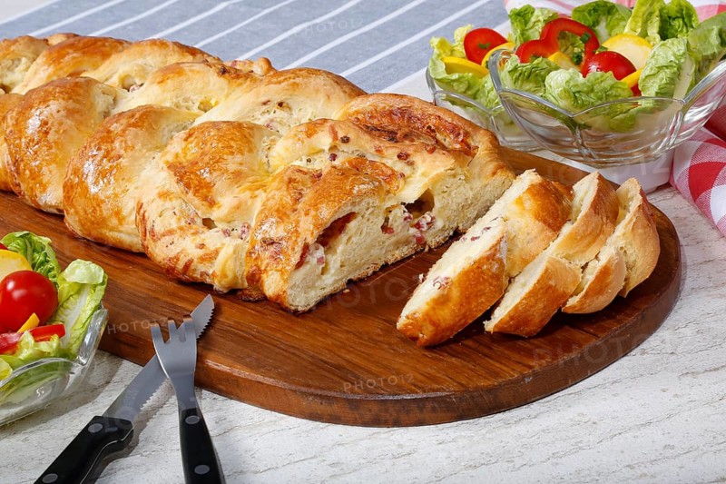 Swabian cuisine, hearty yeast plait with smoked meat, salty wreath bread, yeast yeast dough pastry, arranged on wooden board, baked, grandmother's kitchen, regional, home cooking, typical Swabian reinterpreted, traditional cuisine reinterpreted, salad in the back, small bowl, food photography, studio, Germany, Europe