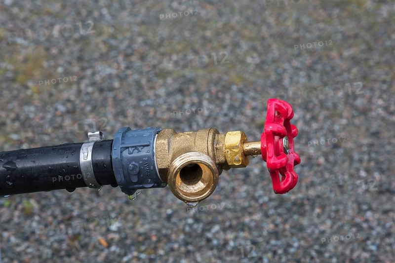 Close-up of black plastic garden hose main water supply connecting pipe with brass fitting and red tap, Quebec, Canada, North America