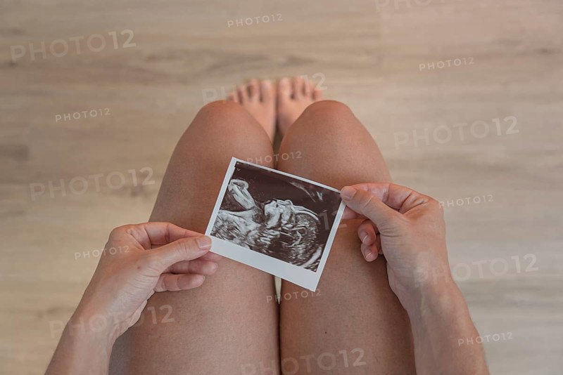 An ultrasound image is held above the knees, symbolising new life, wooden floor background