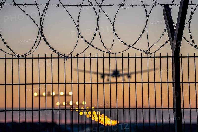 Symbolic image security at the airport, outer fence at Düsseldorf International Airport, steel wire fence, with S-wire rolls, NATO wire, on the top of the fence, aeroplane approaching, sunset, North Rhine-Westphalia, Germany, Europe