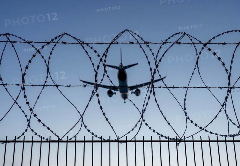 Symbolic image security at the airport, outer fence at Düsseldorf International Airport, steel wire fence, with S-wire rolls, NATO wire, on the top of the fence, aeroplane approaching, sunset, North Rhine-Westphalia, Germany, Europe
