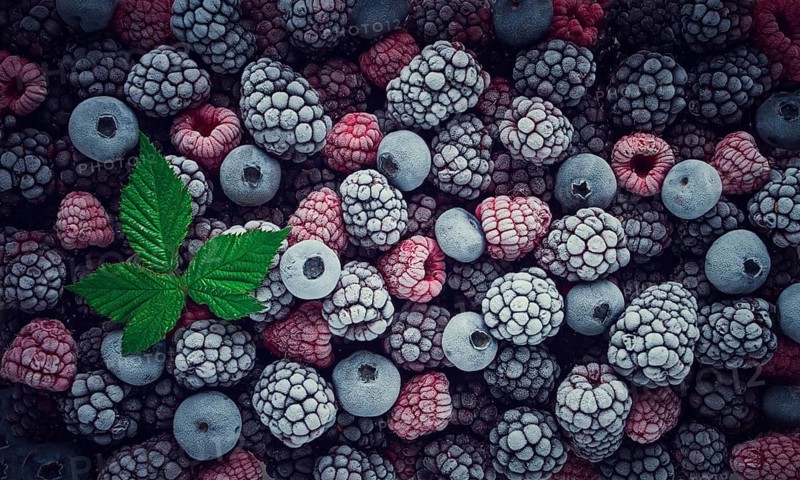 A close-up view features an array of frozen raspberries and blackberries, showcasing their unique textures. A fresh green leaf adds a pop of color to the scene, enhancing visual appeal