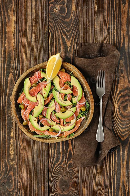 Overhead view of salad with fresh salmon, avocado and onion served in a wooden bowl on a rustic wooden table