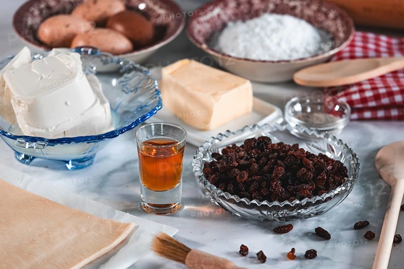 Baking ingredients such as sultanas, sugar, curd cheese and eggs on a kitchen table show a traditional baking preparation