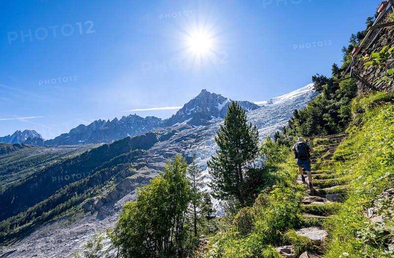 Hiker on hiking trail La Jonction, view of glacier Glacier des Bossons with sun star, behind summit of Aiguille du Midi, Chamonix, Haute-Savoie, France, Europe