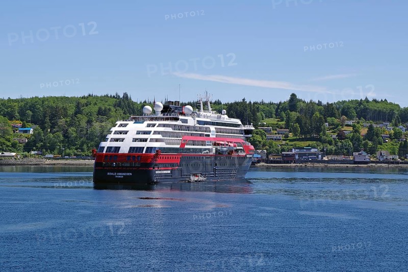 A large Hurtigruten ship sails along a forested coastline under a clear sky, Cormorant Island, Vancouver Island, National Park, Pacific Ocean, British Columbia, Canada, North America