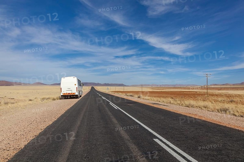 A bus on a deserted country road through a wide, dry landscape under a blue sky, national road B4 near Garub, Namibia, Africa