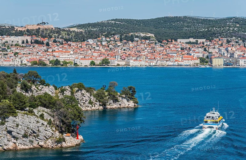 A boat moves through the blue water with a view of a built-up coastal landscape, St Anthony's Channel, Šibenik, Sibenik, Dalmatia, Croatia, Europe