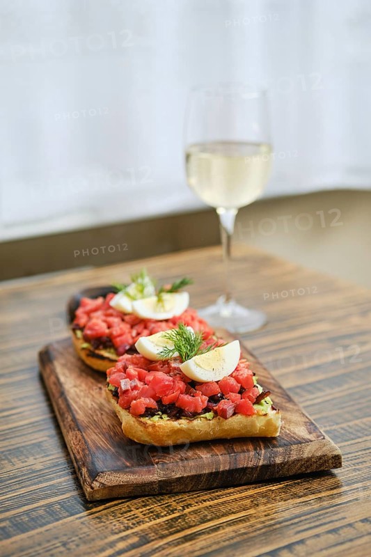 A wooden serving board holds two generous portions of bruschetta topped with diced salmon and egg slices