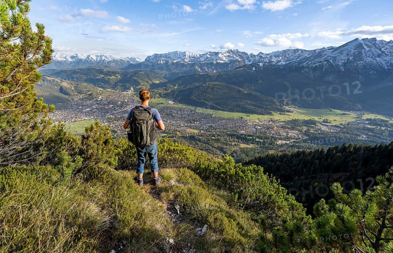 Mountaineer on a narrow hiking trail between mountain pines, view of Garmisch-Partenkirchen and mountain panorama, hike to Kramerspitz, in autumn, Ammergau Alps, in autumn, Bavarian Alps, Bavaria, Germany, Europe