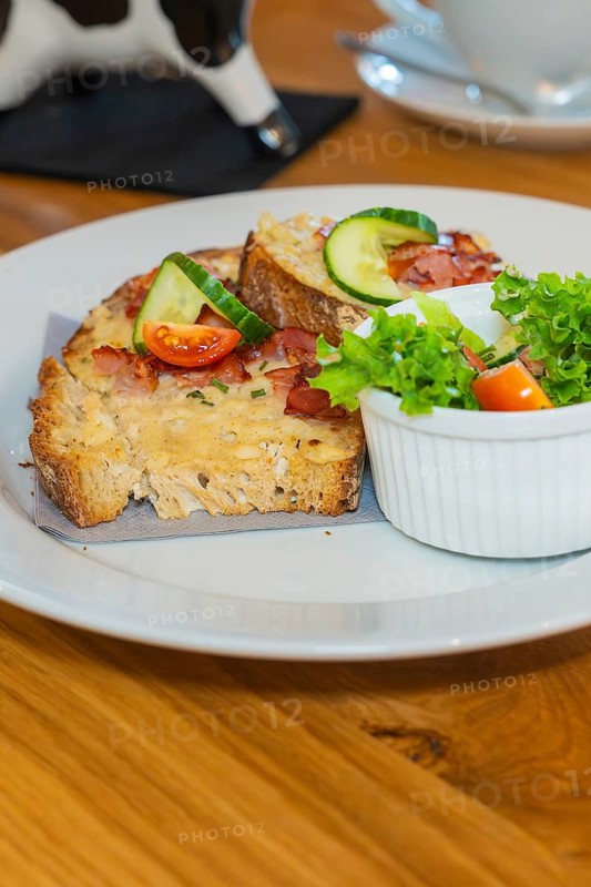 Close-up of toast with melted cheese and ham, decorated with cucumber and tomato, next to it a small salad, autumn creations, Cafe Kuh, Deckenpfronn, Black Forest, Germany, Europe