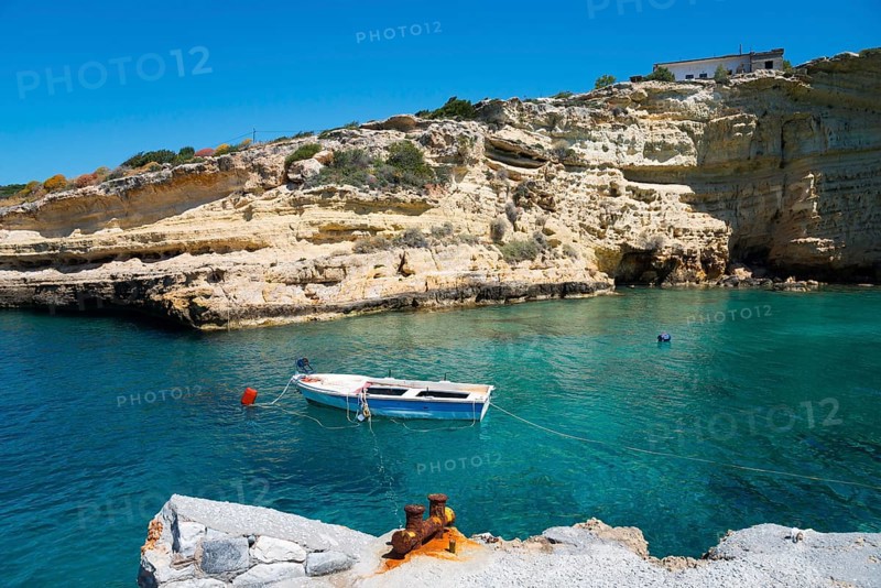 Lonely boat on calm water in front of high rocks under a clear sky, Mezapos, Mani, Peloponnese, Greece, Europe