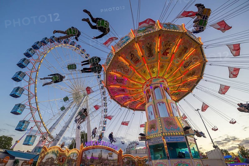 A funfair at dusk with illuminated chain carousel and Ferris wheel, Europa Rad, rides, wave flight, Cannstatter Wasen, folk festival, Bad Cannstatt, Stuttgart, Baden-Württemberg, Germany, Europe