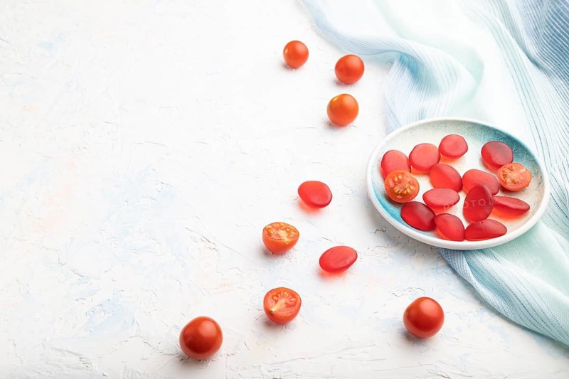 Jelly tomato candies on white concrete background and blue linen textile. copy space, side view