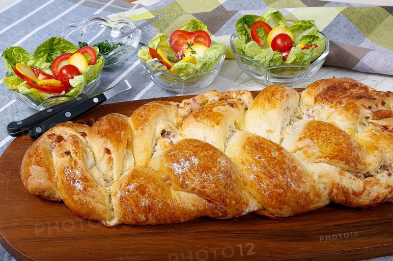 Swabian cuisine, hearty yeast plait with smoked meat, salty wreath bread, yeast yeast dough pastry, arranged on wooden board, baked, grandmother's kitchen, regional, home cooking, typical Swabian reinterpreted, traditional cuisine reinterpreted, salad in the back, small bowl, food photography, studio, Germany, Europe