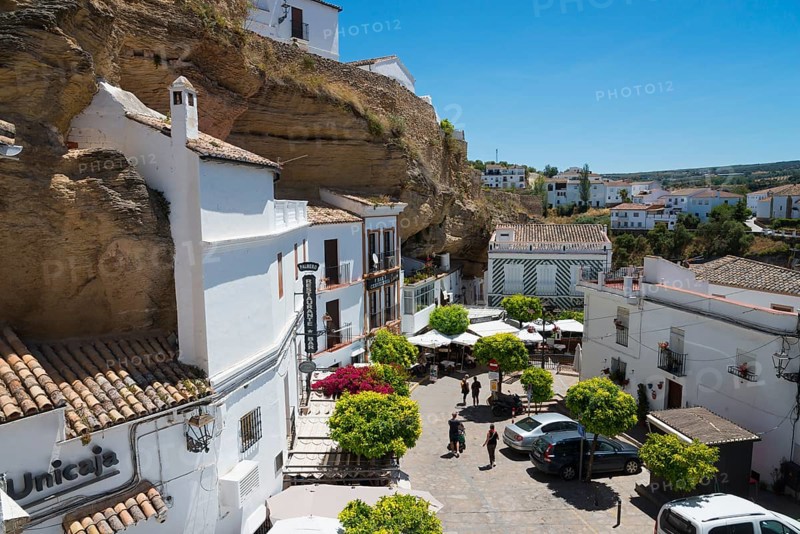 Square with cars and cafés in Setenil de las Bodegas under rocks with white houses, blue sky, cave dwellings, Setenil de las Bodegas, Cadiz, Andalusia, Spain, Europe