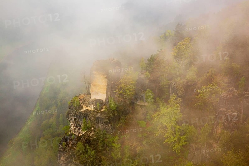 The bright Wartturm above the Elbe river, hidden in dense fog. Seen from the Bastei rocks near the village of Rathen in Saxon Switzerland National Park, Saxony, Germany. On November 22, 2000 the Wartturm was the scene of a spectacular rockfall