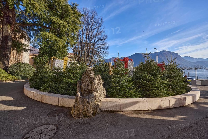 Christmas market in Piazza Manzoni, roundabout with Christmas trees, lake, mountains, trees, blue sky, veil clouds, Lake Lugano, street Riva Giocondo Albertolli, Lugano, district Lugano, canton Ticino, Switzerland, Europe