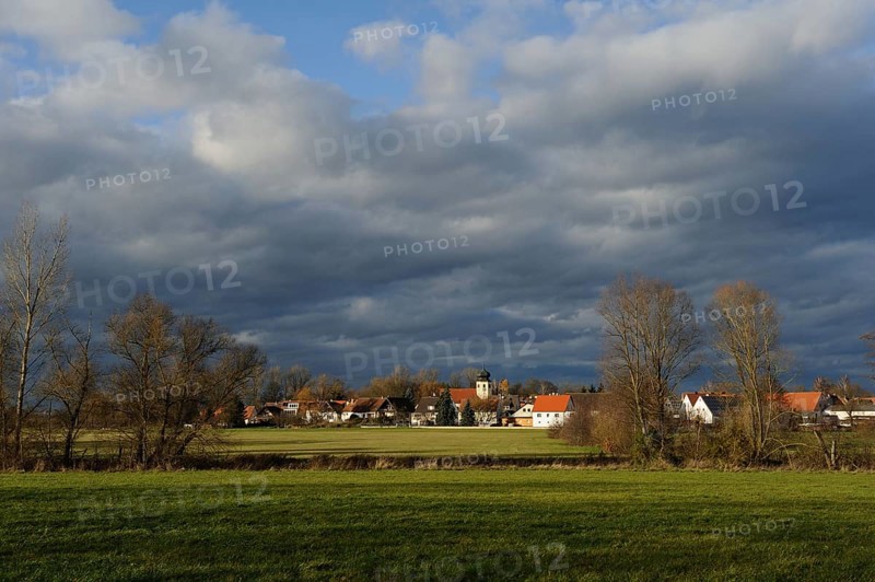 Vast landscape with a small village under a dramatic cloudy sky, surrounded by green meadows and bare trees, Muhr am See, Altmühlsee, Franconia