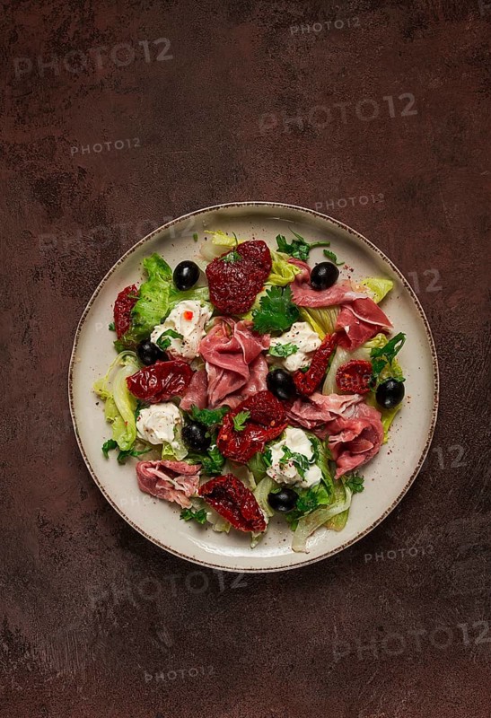 Salad with dried tomatoes, prosciutto, soft cheese, olives, homemade, top view